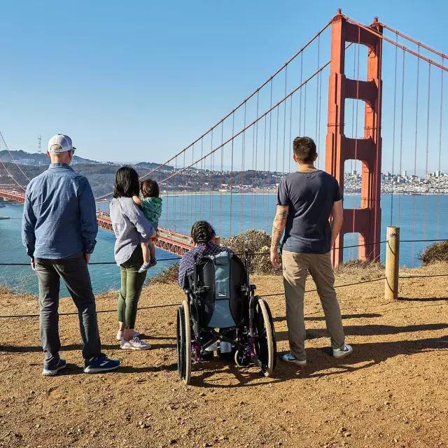 一群人, 包括一个坐轮椅的人, 从后面看, 从马林岬俯瞰金门大桥。.